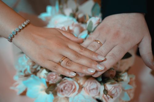 Free A romantic close-up of newlywed hands displaying wedding rings over a floral bouquet. Stock Photo