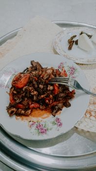 A tasty dish of grilled meat with vegetables on a floral plate, served with bread.