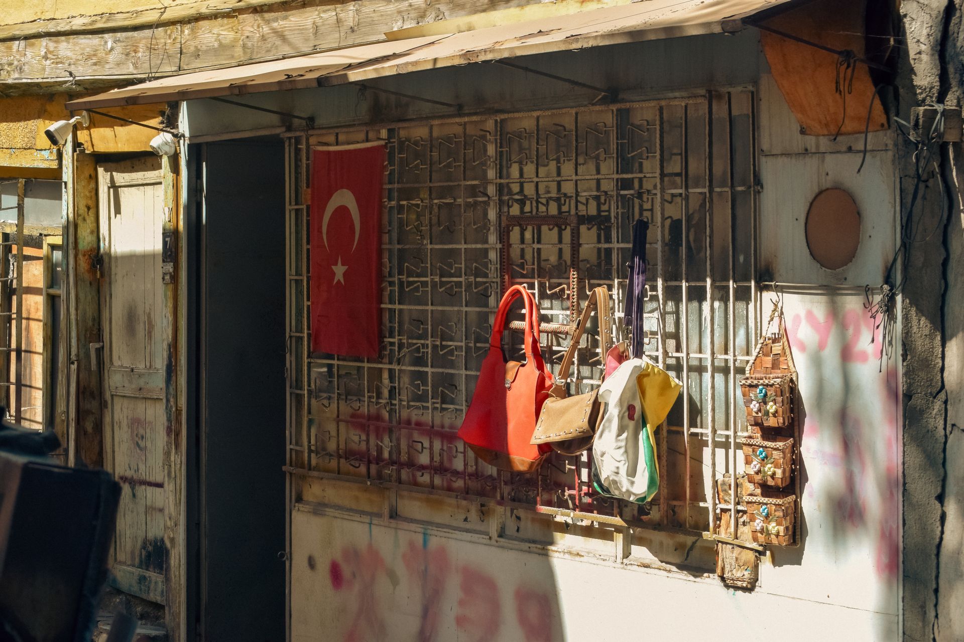 Old shop facade with Turkish flag and handbags on display, bathed in sunlight.