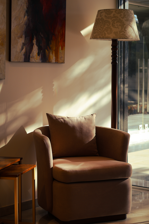Free Elegant brown armchair by a window with sunlight casting shadows in a modern interior. Stock Photo