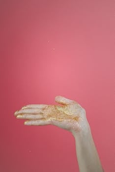 在粉红色的工作室背景下，一只沾满金色闪光的手举了起来