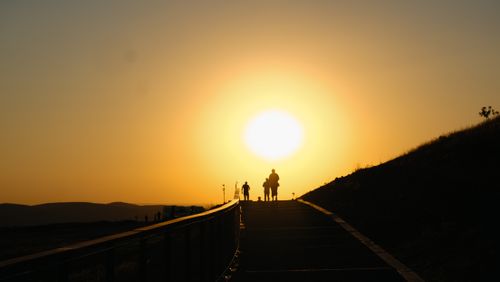 Free Silhouetted people walk toward setting sun on a hill, creating a dramatic sunset scene. Stock Photo