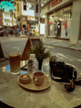 Outdoor café table with coffee, water, and camera in a vibrant city street.