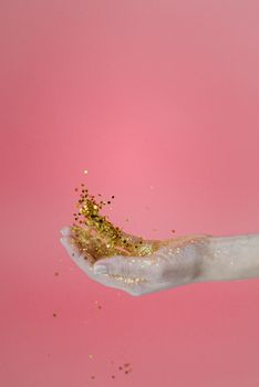 一只精致的手优雅地在充满活力的粉红色背景上洒下金色闪光