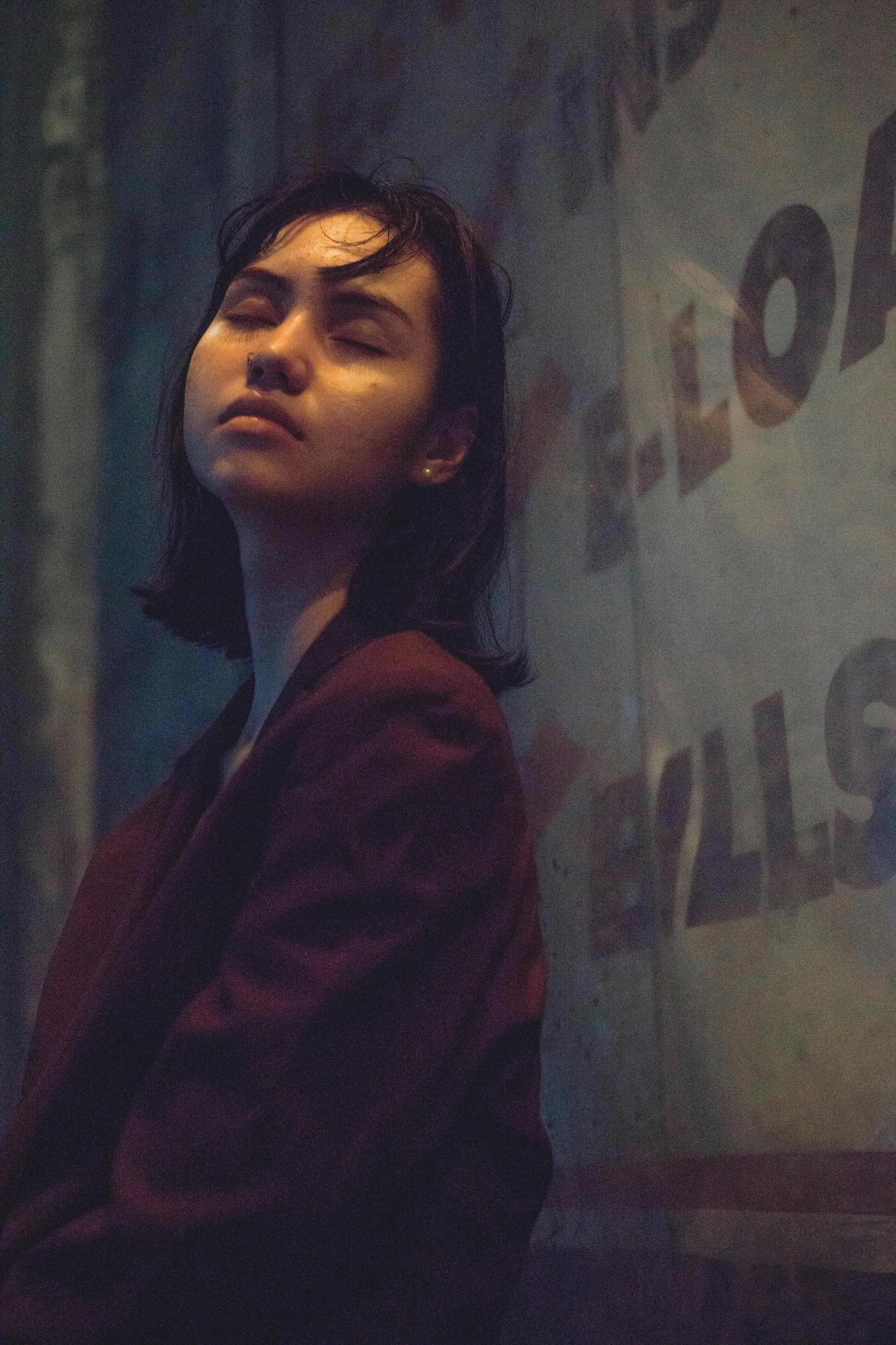 一位女士在光线昏暗的城市街角倚墙沉思，散发着时尚而忧郁的氛围