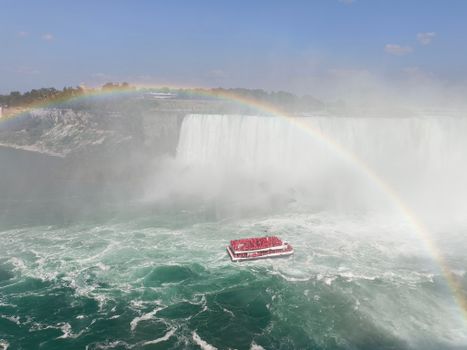 A breathtaking view of Niagara Falls with a tour boat and a vibrant rainbow.