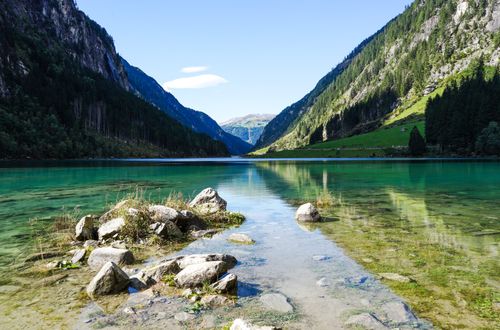 Free Beautiful alpine lake surrounded by lush mountains under a blue sky, offering a tranquil landscape. Stock Photo