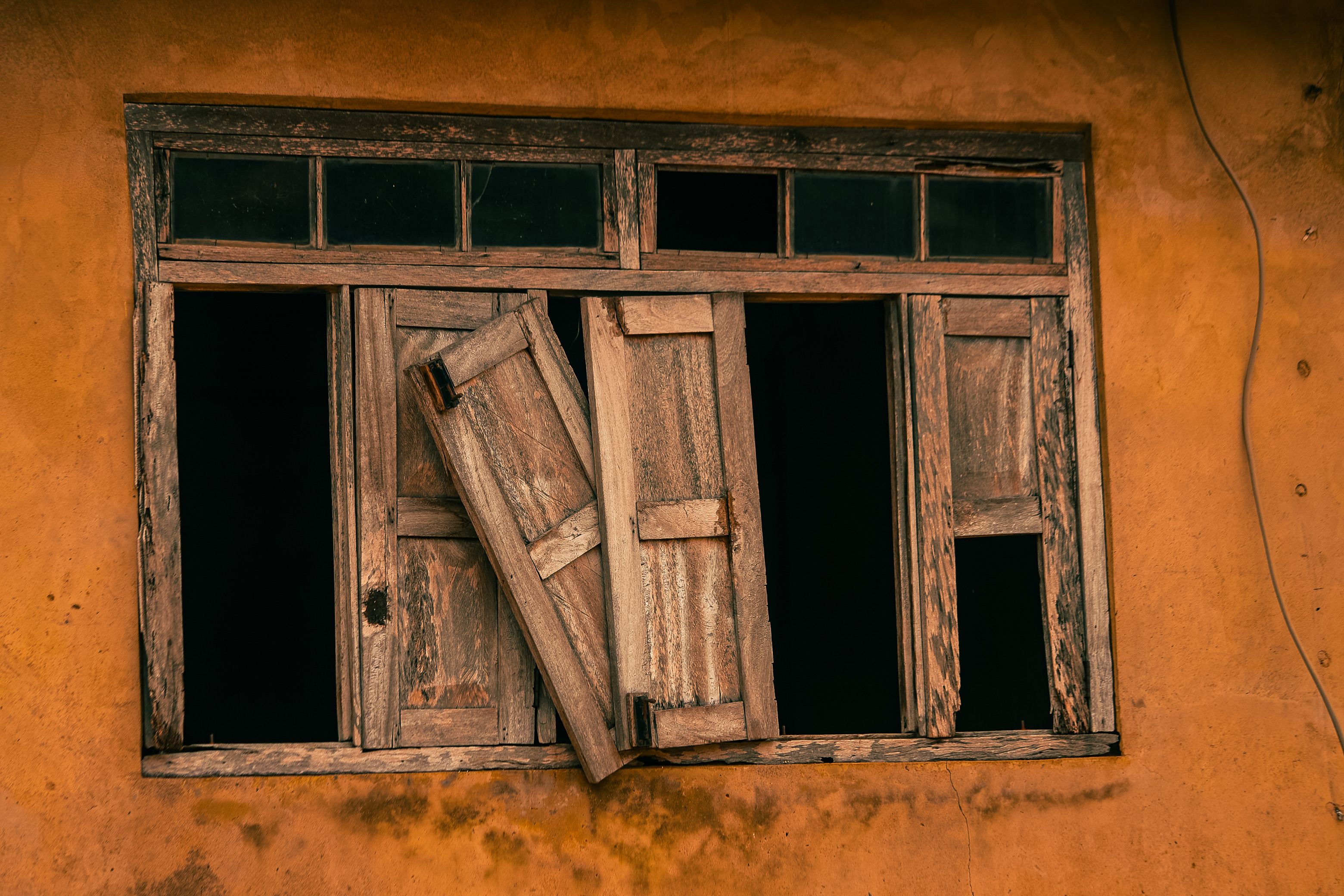 Aged wooden window on an orange wall in Nigeria, highlighting rustic architecture.