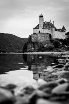 Black and white photo of a historic castle reflecting in a tranquil river.