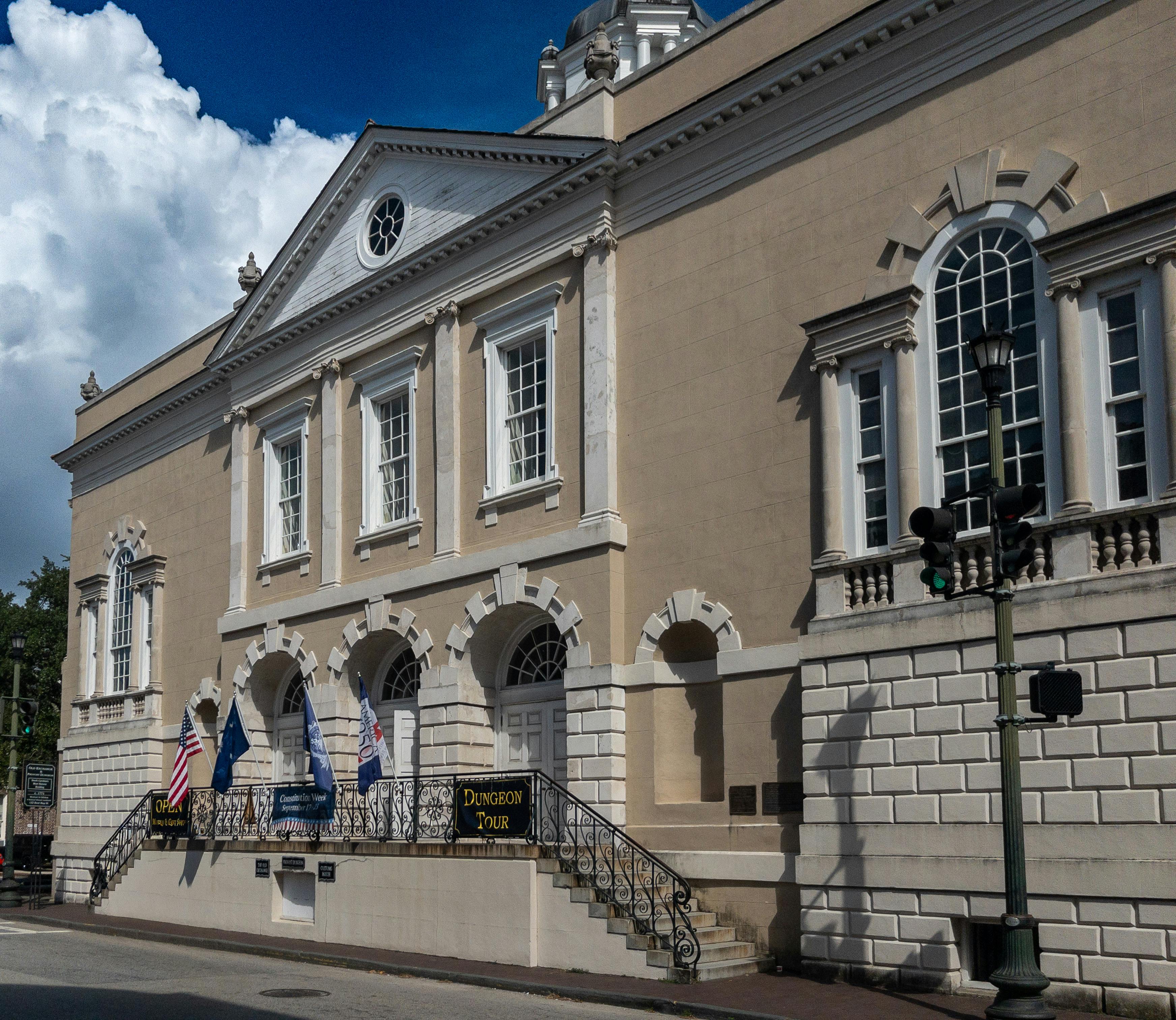 Classic colonial architecture of a historic building in Charleston featuring flags and a dungeon tour sign.