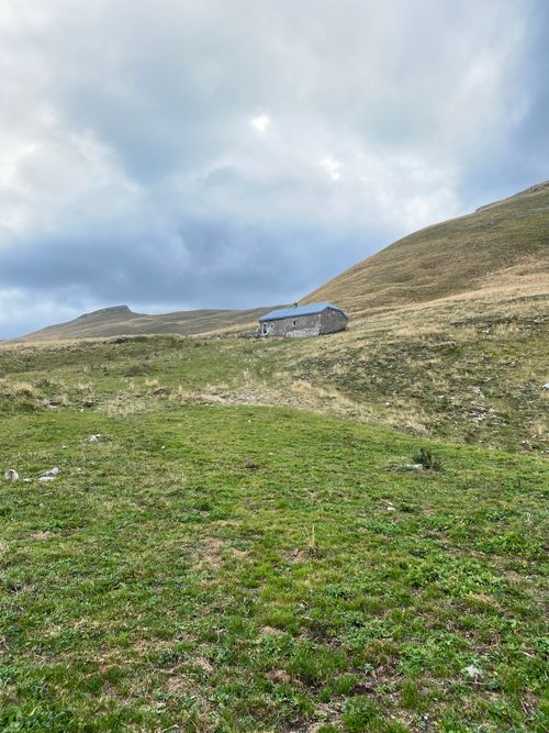 Free Remote mountain hut scene with dramatic clouds and rolling hills, a serene landscape. Stock Photo