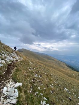 Lone hiker traversing a dramatic mountain path under cloudy skies.