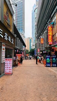 Busy urban street in Chongqing with people, shops, and skyscrapers showcasing vibrant city life.