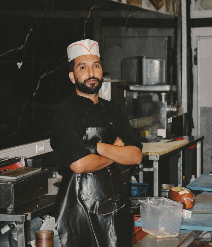 Chef in a black uniform and paper cap standing with arms crossed in a restaurant kitchen