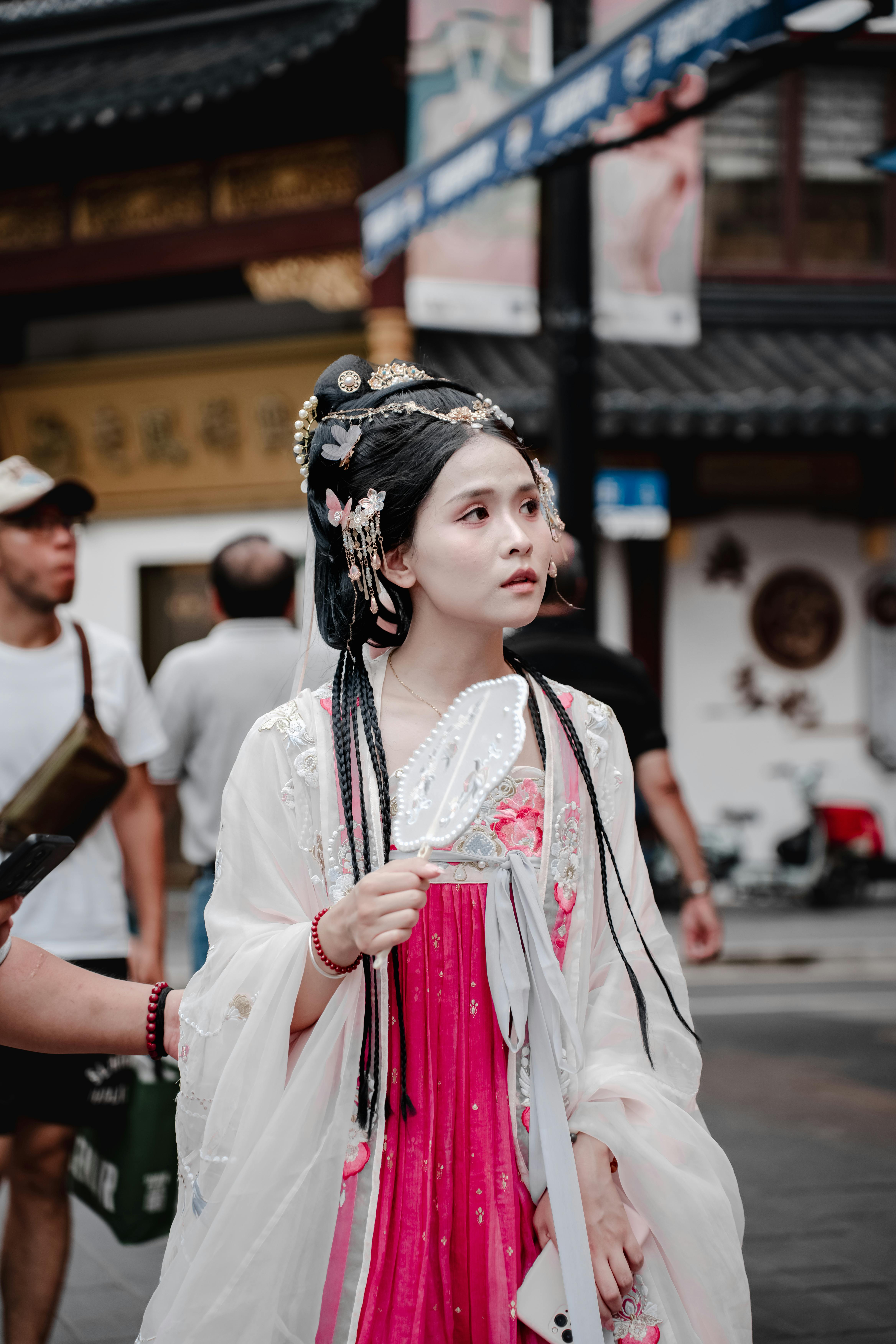 A young woman in traditional Chinese Hanfu attire walks through a bustling outdoor market.