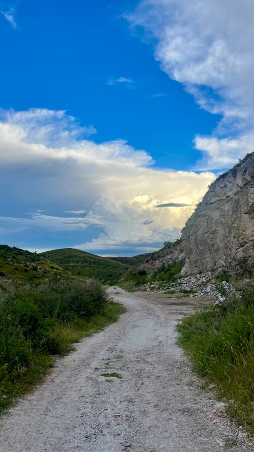 Free A serene rocky pathway winds through lush green hills under a vibrant blue sky. Stock Photo