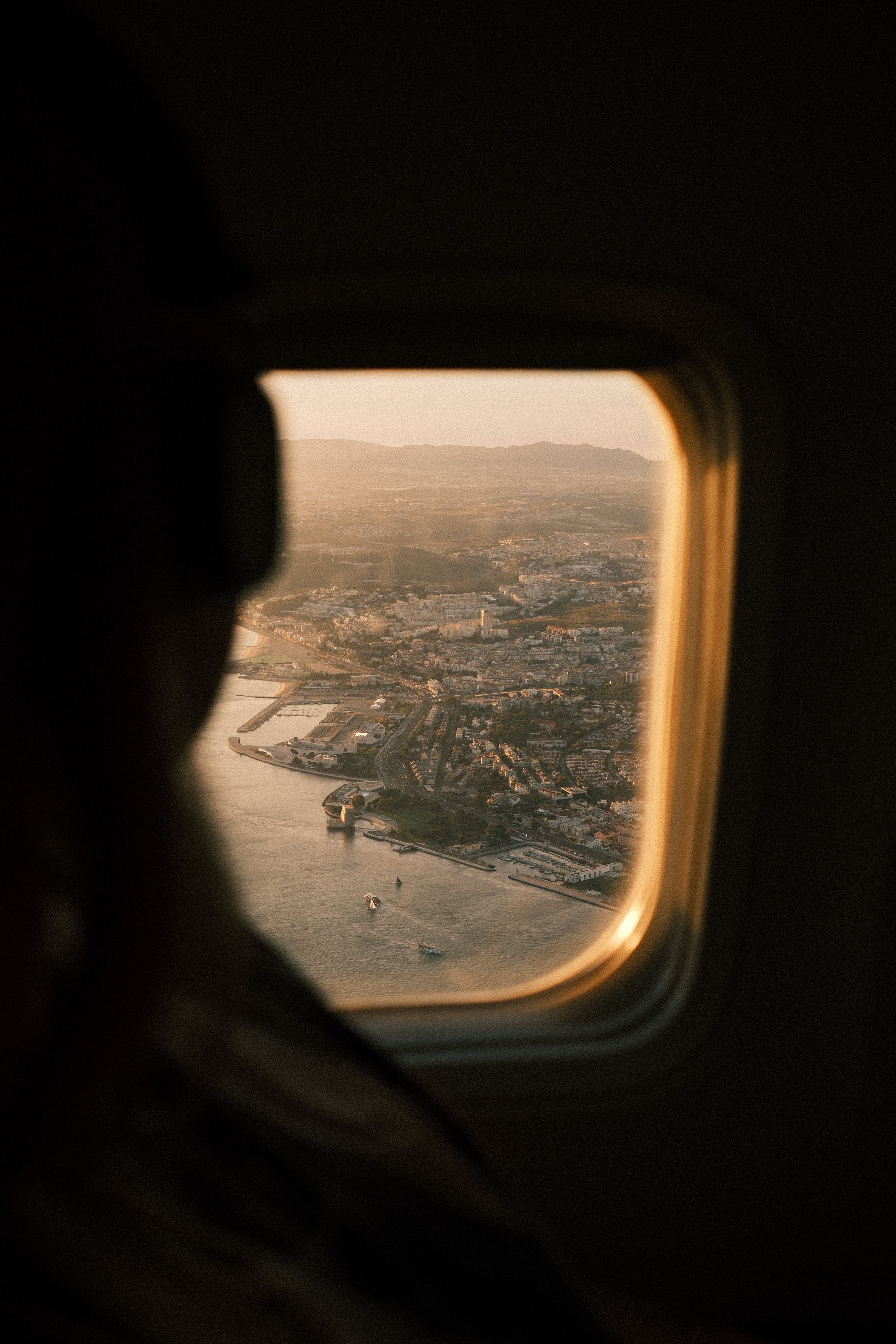 Stunning aerial view of Lisbon, Portugal at sunset through a plane window, capturing the cityscape and ocean.