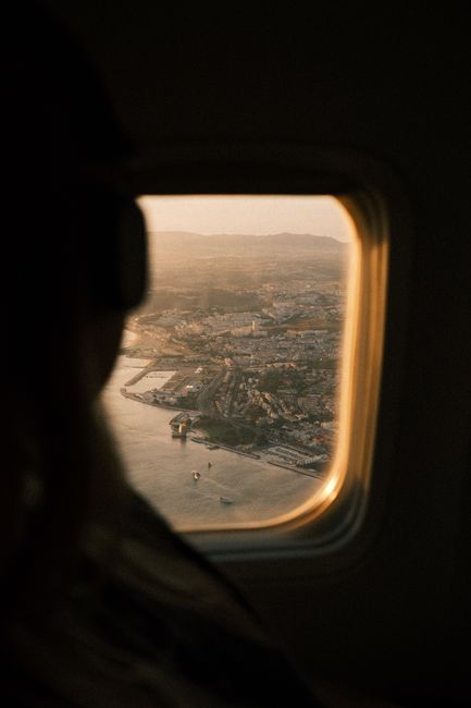 Stunning aerial view of Lisbon, Portugal at sunset through a plane window, capturing the cityscape and ocean.