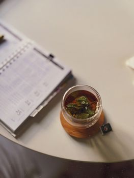 Glass cup of green tea with mint on an office desk beside an open calendar.