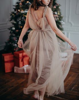 一位女士身着优雅礼服，姿态优雅地站在装饰着礼物的圣诞树旁