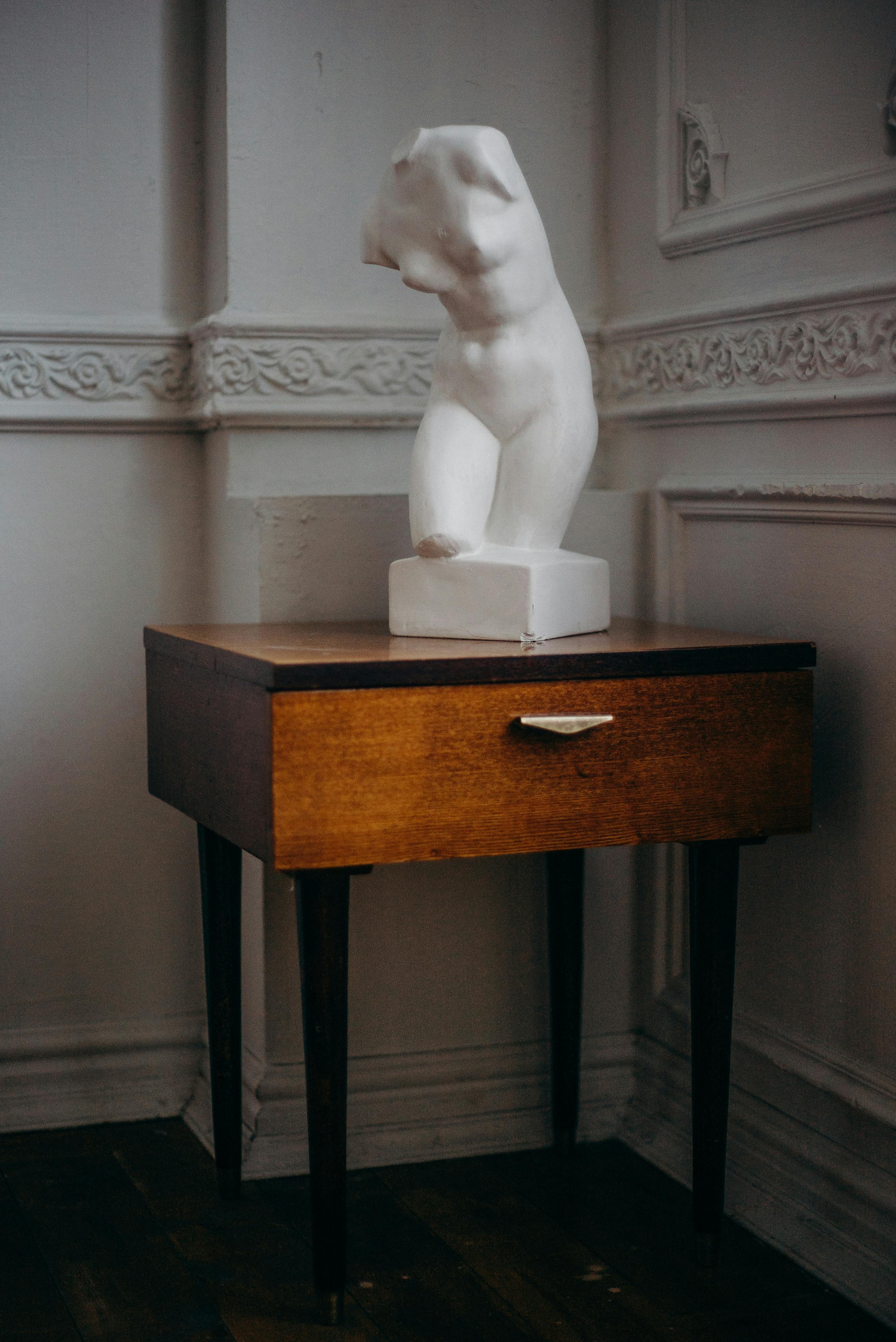 复古木桌上摆放着一尊白色躯干雕塑，置于设计优雅的内部空间中