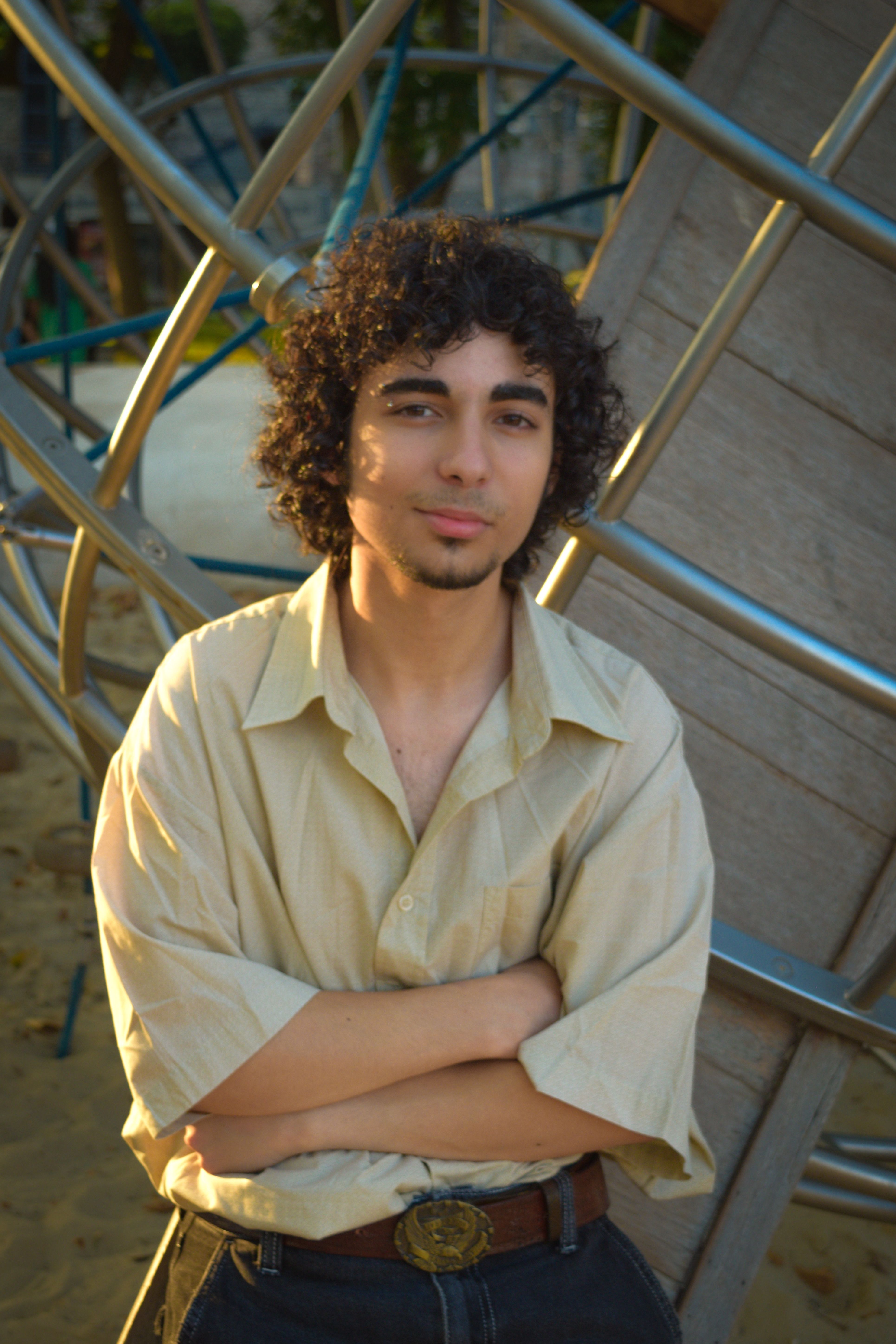 Casual young man with curly hair posing outdoors in a playground setting.