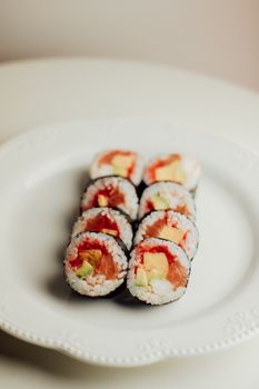 Tasty salmon sushi rolls with avocado and rice served on a white plate. Perfect for food enthusiasts.