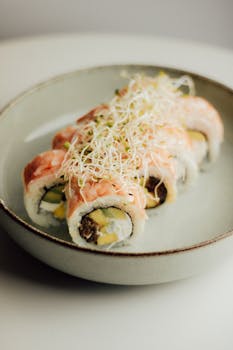 Mouthwatering salmon sushi roll topped with fresh sprouts on a ceramic plate.