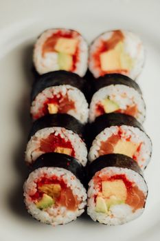 Close-up of salmon sushi rolls with avocado and egg on a white plate, showcasing vibrant colors and textures.