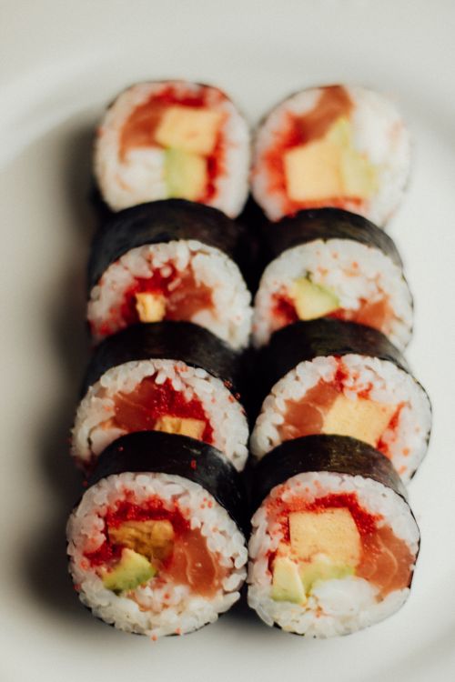 Free Close-up of salmon sushi rolls with avocado and egg on a white plate, showcasing vibrant colors and textures. Stock Photo