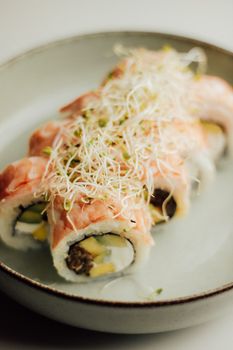 Delicious salmon sushi rolls topped with fresh sprouts, captured on a ceramic plate indoors.