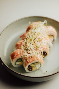 Close-up of a gourmet sushi roll topped with fresh sprouts served in a ceramic dish.
