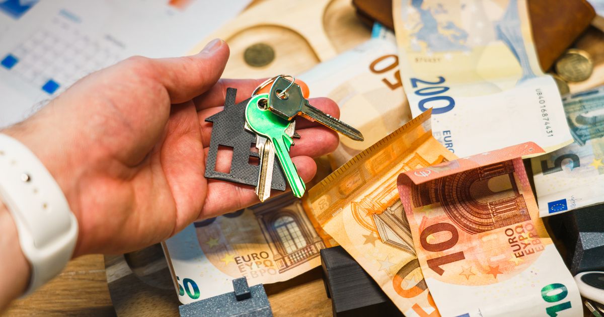 A hand holding house keys over euro banknotes, symbolizing real estate and finance.