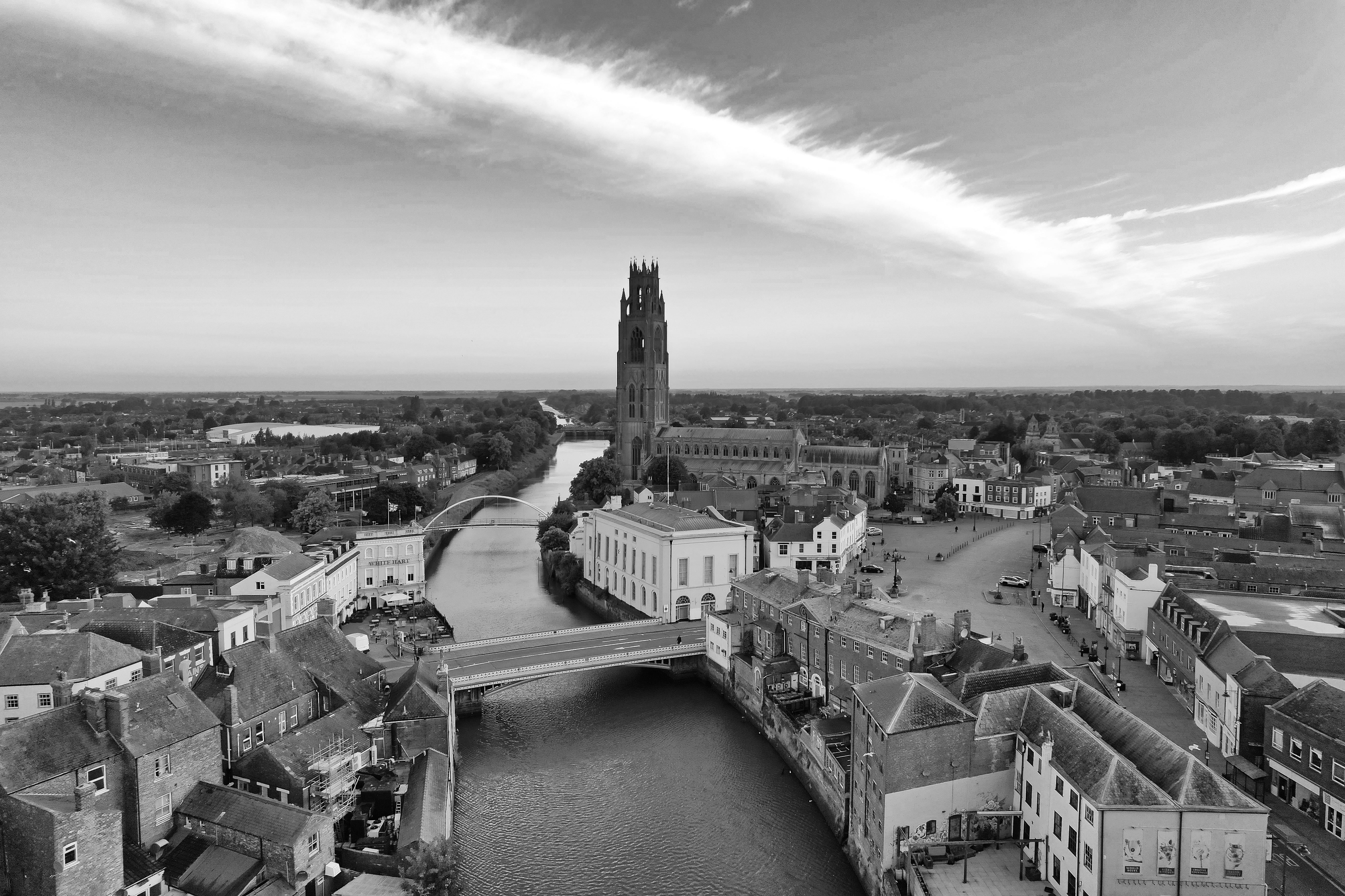 Black and white aerial view of the iconic Boston Stump Tower in Lincolnshire, England, along a serene river.
