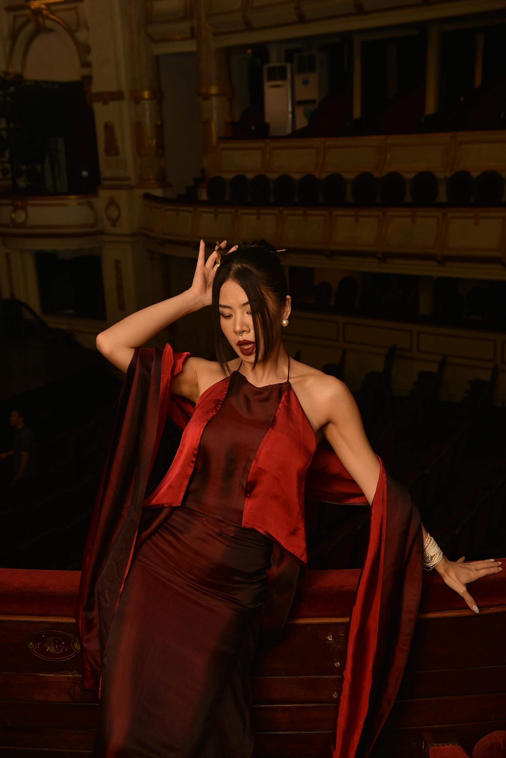 Ücretsiz Tiyatroda şık kırmızı elbiseli kadın zarif bir şekilde poz veriyor. Dramatik bir atmosfer. Stok Fotoğraflar