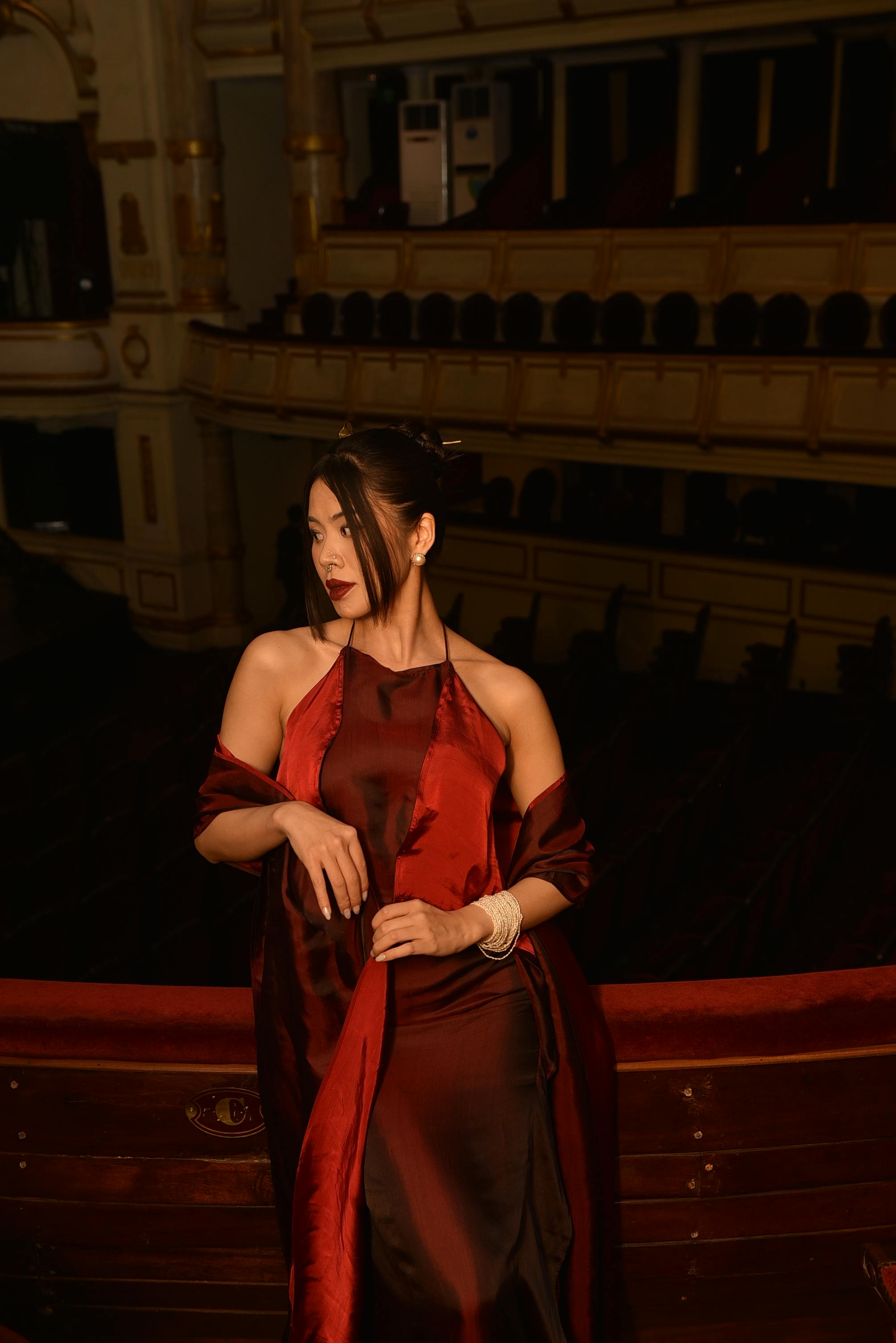 Free Stunning portrait of a woman in a red gown inside a grand theater setting, exuding elegance. Stock Photo