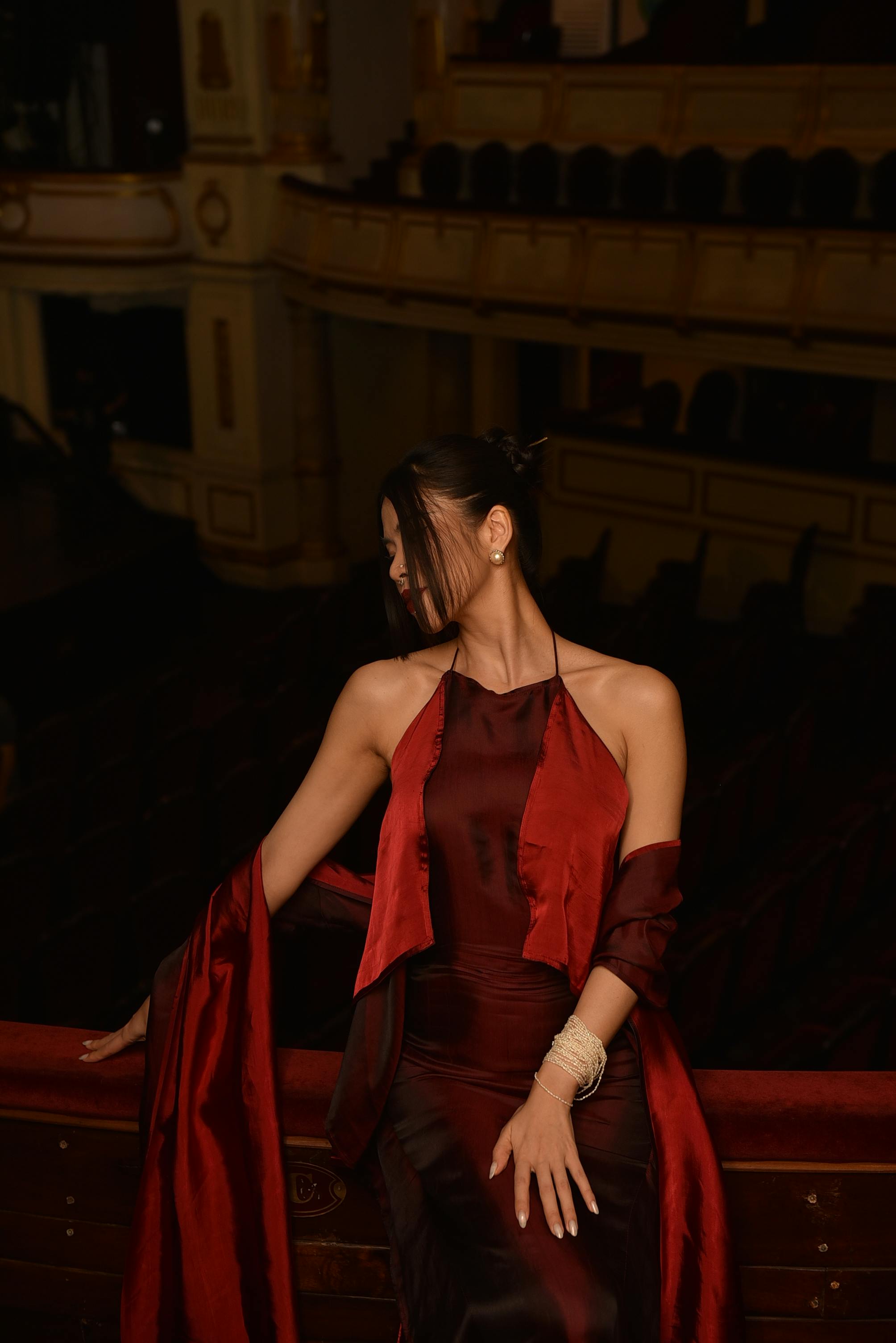 bezplatná Sofistikovaná žena pózuje elegantně na prázdném balkonu divadla v elegantních vínových šatech. Základová fotografie