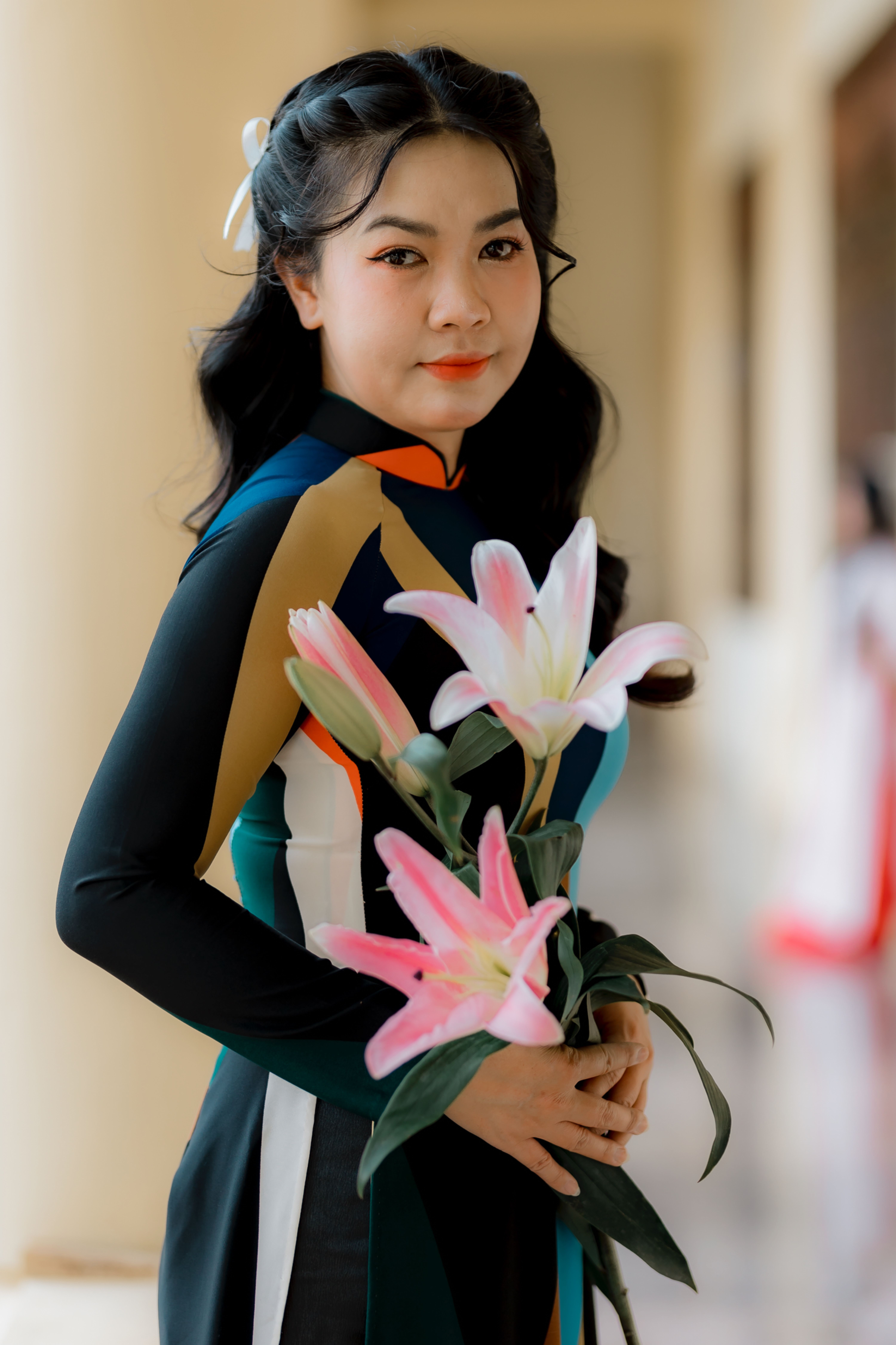 Portrait of a woman in a colorful dress holding pink lilies indoors. Soft focus creates an artistic effect.