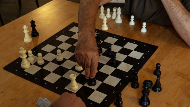 Close-up of hands playing chess on a wooden table, emphasizing strategic moves.