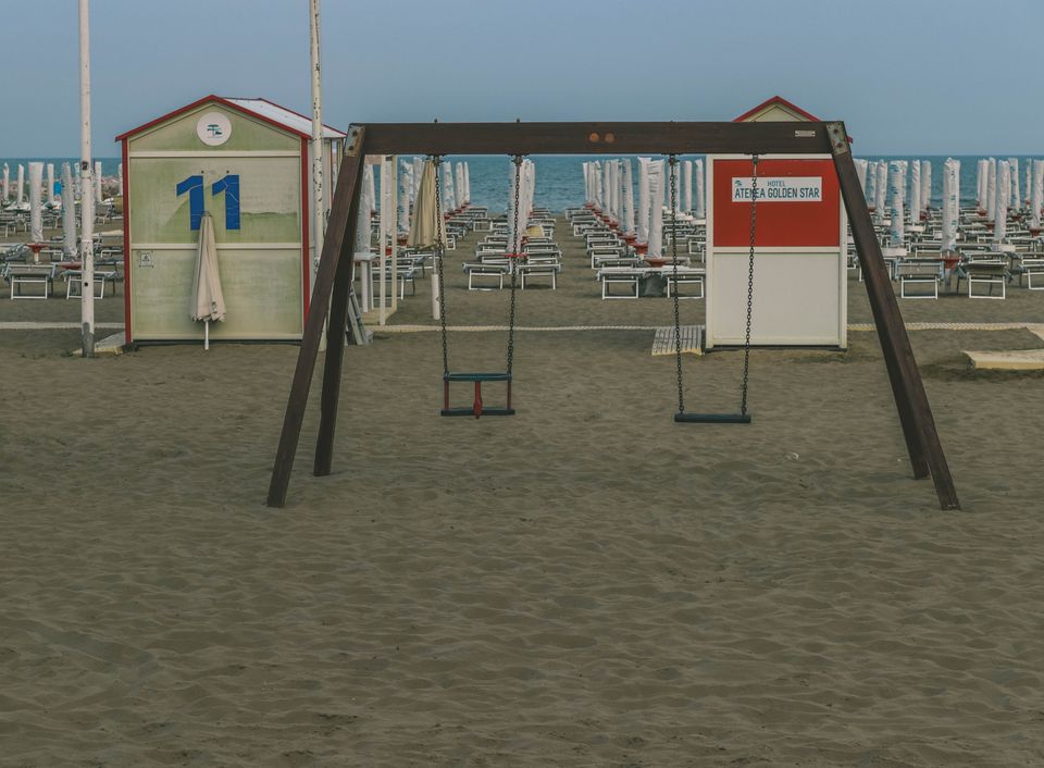 Abandoned swing set on a sandy beach with empty sunbeds and cabanas at sunrise.