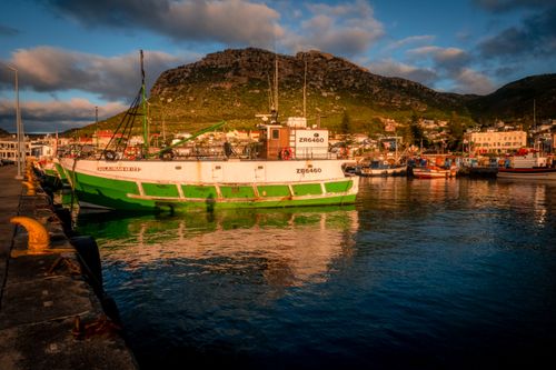 Free Colorful fishing boat in a serene harbor at sunset with mountain backdrop. Stock Photo