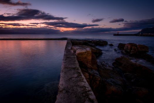 Breathtaking sunrise view over a rocky coastline with a pier extending into the sea.