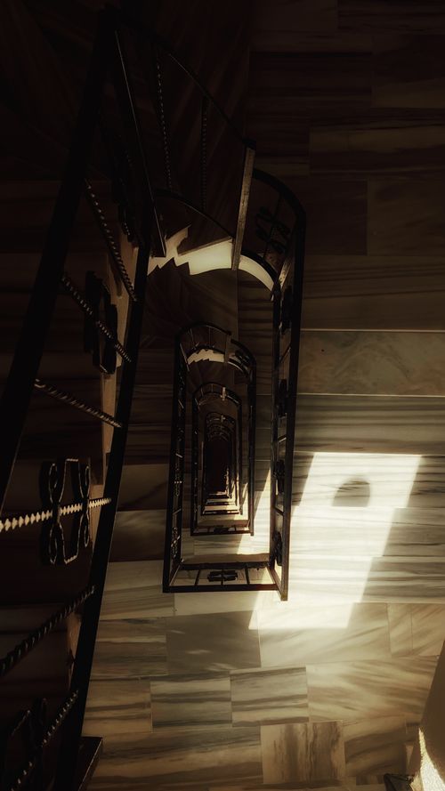 Free A mesmerizing view down a spiral staircase with dramatic light and shadows. Stock Photo