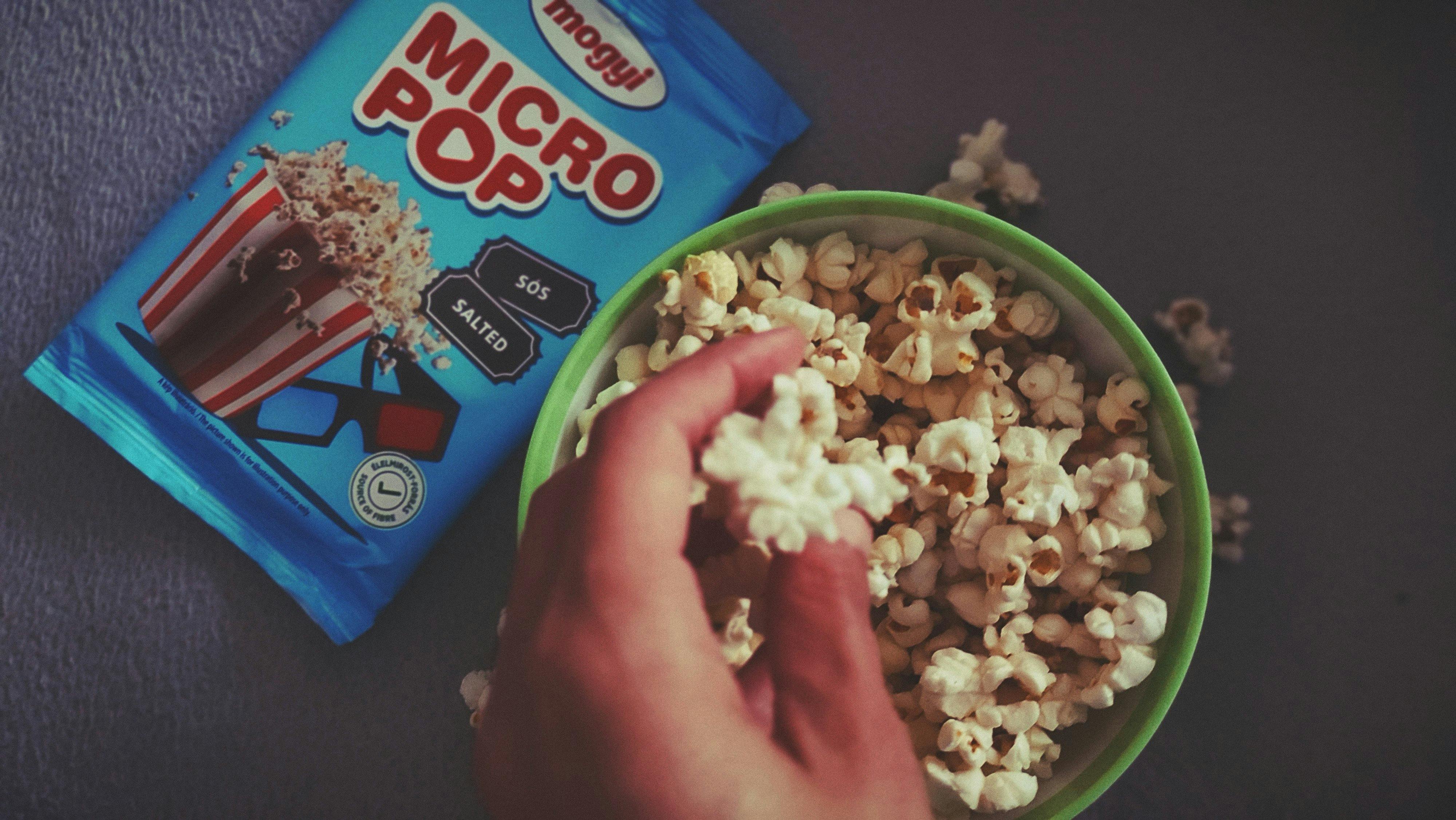 Gratuit Une main tendue vers le pop-corn dans un bol à côté d'un paquet de pop-corn sur une table. Photos