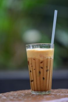 Tall glass of iced coffee with straw in a relaxing outdoor setting, perfect for summer refreshment.