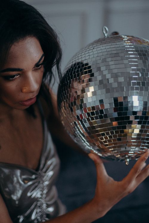 Free Young woman in silver dress holding a sparkling disco ball indoors. Stock Photo