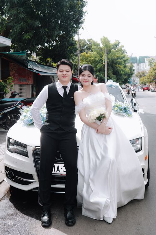 Free A bride and groom elegantly pose by a decorated car on their wedding day outdoors. Stock Photo