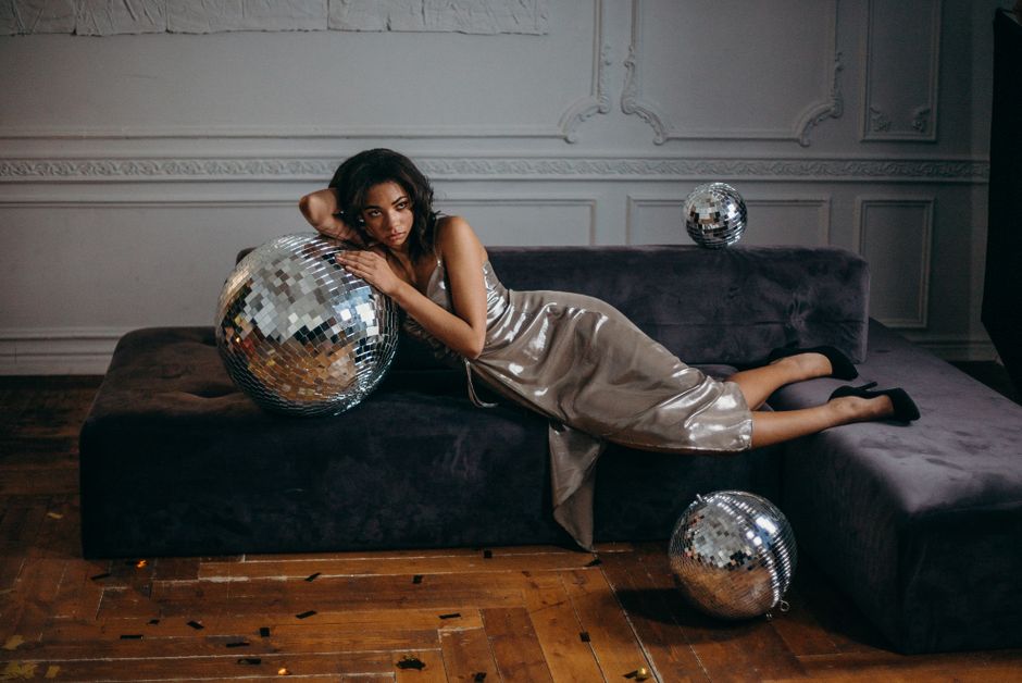 Maximalist Glam decor style interior — Elegant fashion model lying on a couch with disco balls in a stylish indoor setting.