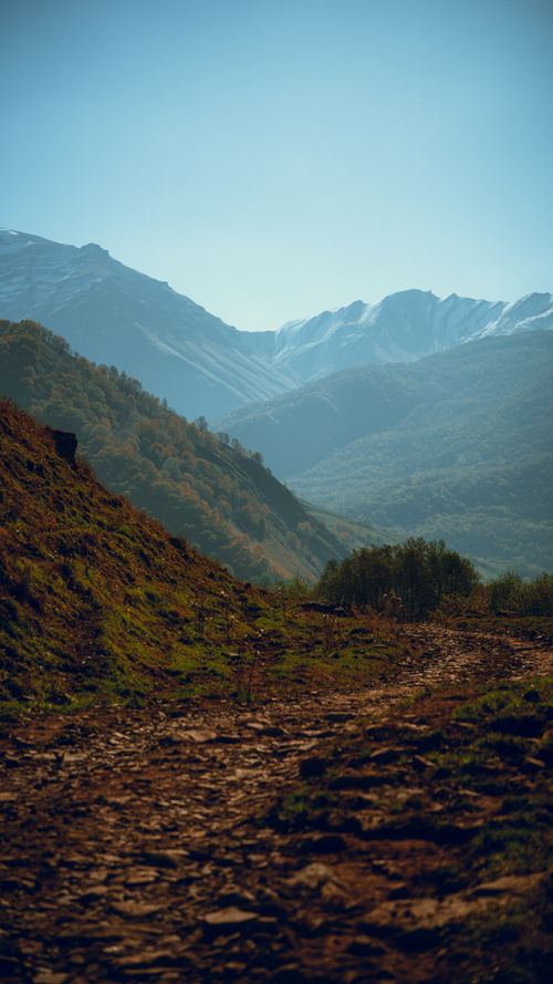 Free A serene mountain path winds through a lush valley beneath snowy peaks. Stock Photo