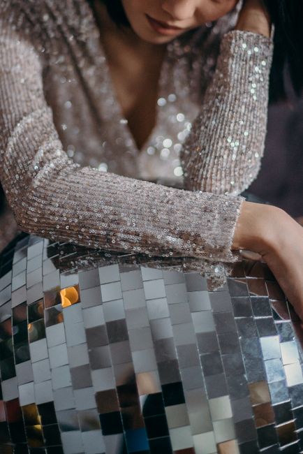 Elegant woman in sequin dress posing with a large disco ball, evoking a glittering party vibe.